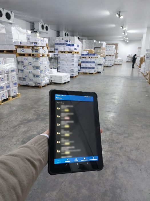 Mano con una tablet que muestra una aplicación de inventario dentro de una cámara.